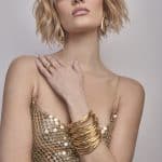 Fashion model with blonde wavy bob hairstyle and gold accessories.
